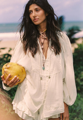 a-woman-on-a-beach-wearing-a-loose-white-bohemian-style-blouse-and-holding-a-yellow-coconut